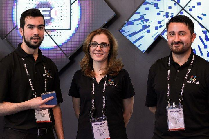 3 Userful employees, with one of them holding a Userful adapter, in front of two different artistic video walls