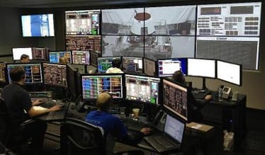 A control room with workers at their workstations and a video wall displaying live footage and data