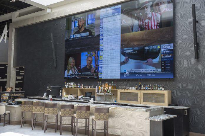 Bar and bartools, large video wall with ads, news channels, and flight information at the Drift Kitchen and Bar