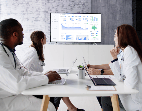 Doctors meeting in meeing room to go over data dashboard on screen