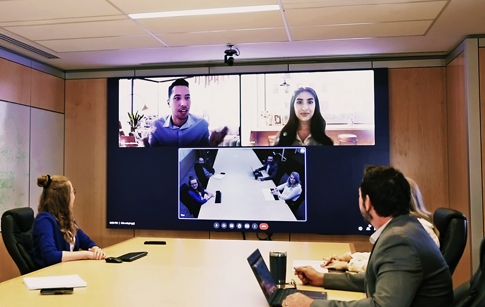 Co workers sitting around bored room table on a video call with two other co workers.