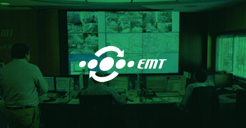 EMT employees monitoring transit operations through their workstations and a video wall displaying live camera footage, transit maps, and websites with green overlay and logo
