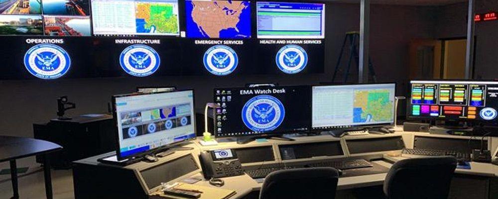 EMA's empty control center with workstations and video wall displaying photos, data, and maps