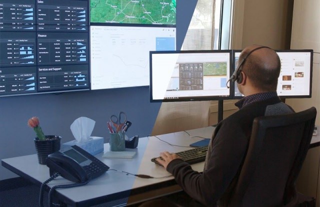 Employee in control room at his work desk typing, looking at a video wall displaying data dashboards and maps