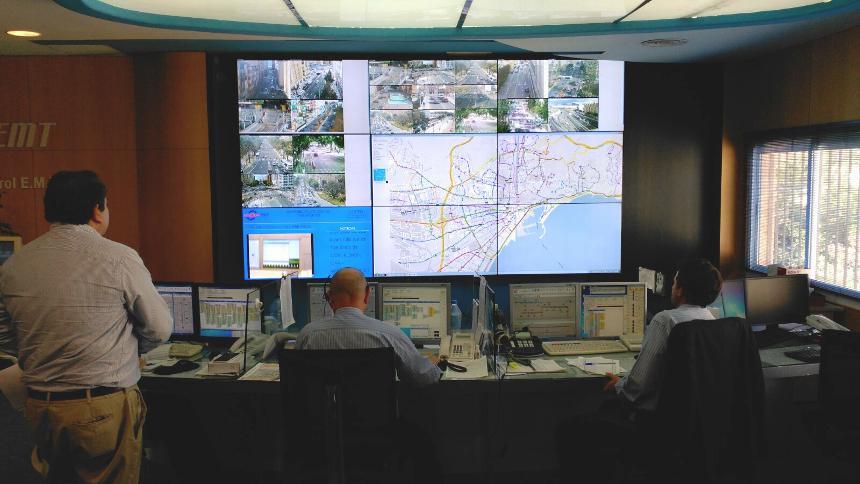 EMT Control Center with workers monitoring transit conditions through their workstations and a video wall displaying transit routes, live footage, and data