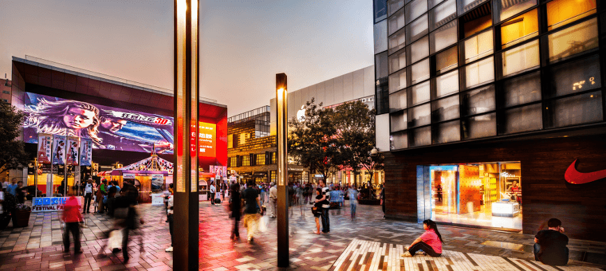 Shopping center, with video wall displaying a movie advertisement, and many people walking around in the evening